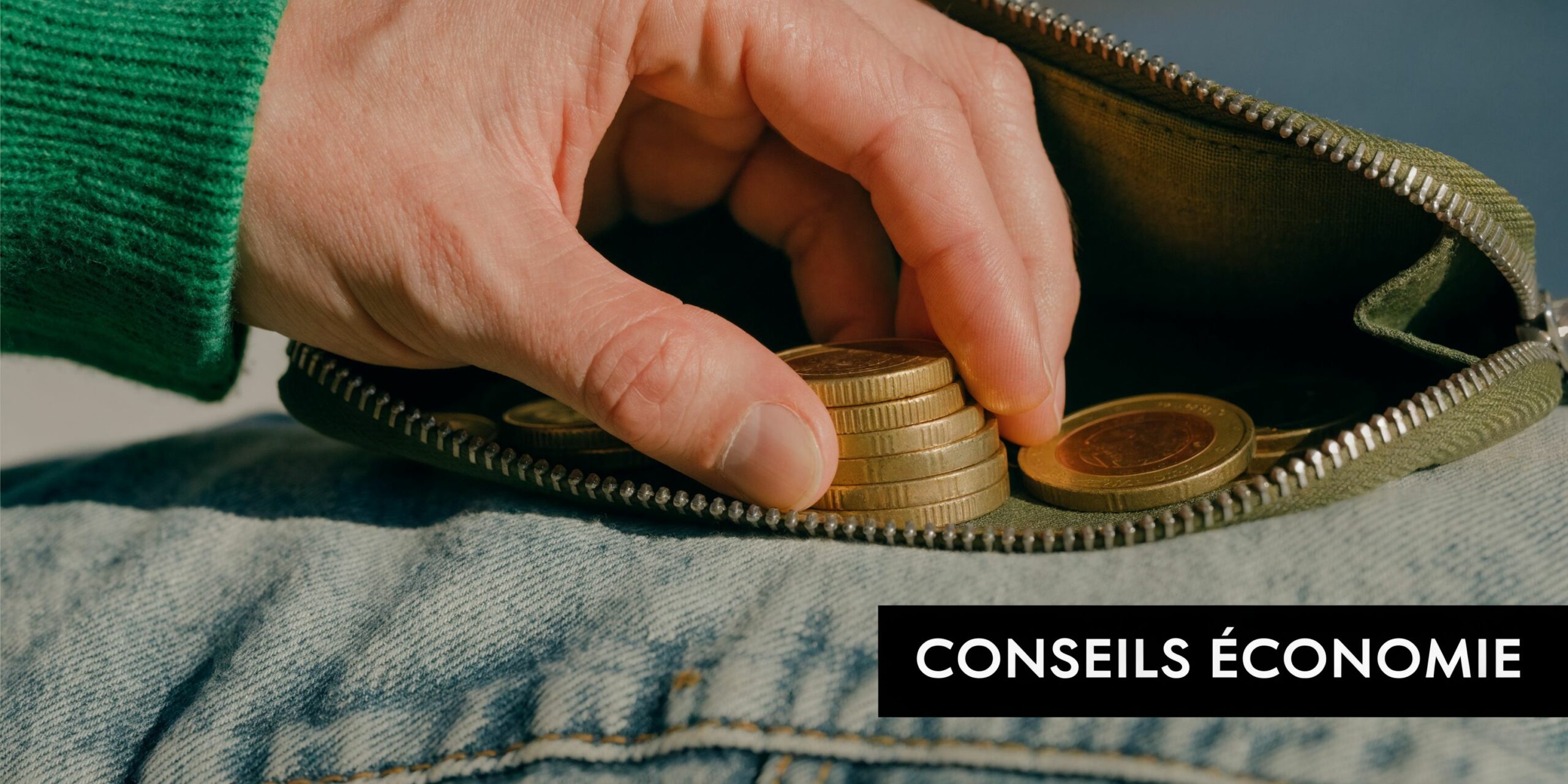 Une main retirant des pièces de monnaie d'un petit portefeuille en tissu posé sur un jean bleu